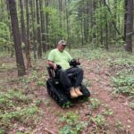 Randy in his new EcoRover track chair going down a path in the woods