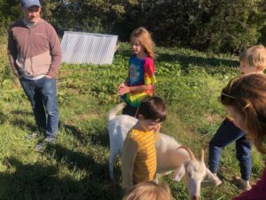 David (L), Oscar (Middle background), Ca;lvin (front center) and Cooper (R) and others spending a moment with our goat, Peanut