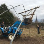 Wooden rig built in tractor loader bucket to lift greenhouse arch poles